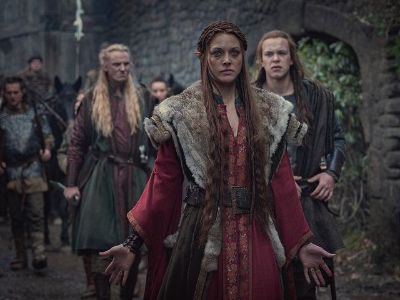 The picture shows Mecia Simson in a red dress as she is walking and men are walking behind her.